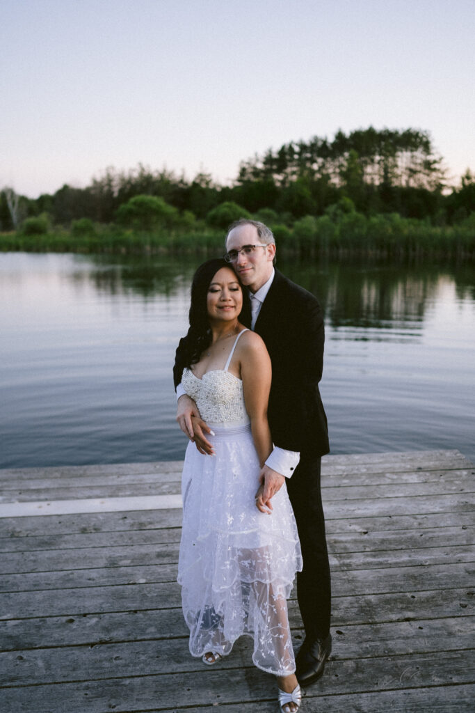 A couple embracing on a wooden pier by a lake at dusk.