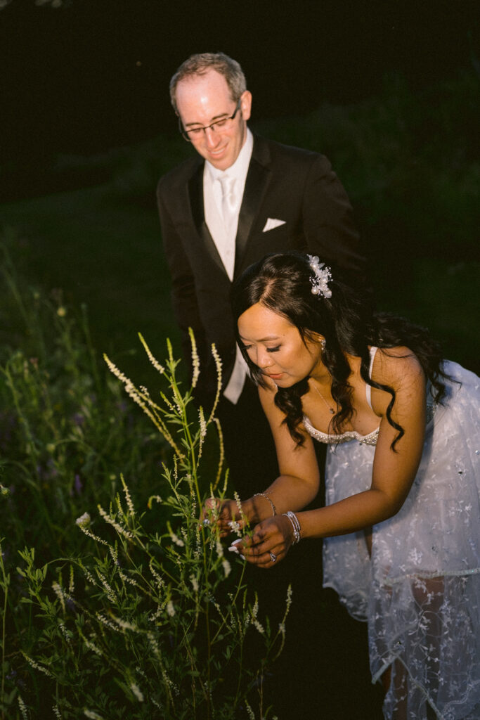 A bride and groom walking together and smiling in a twilight outdoor setting.