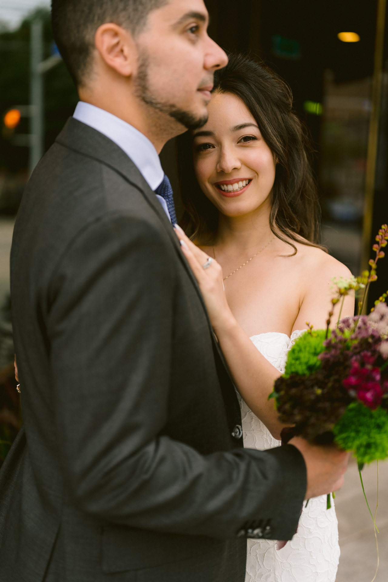 A couple in wedding attire sharing a moment on a city street, with the bride holding a bouquet.
