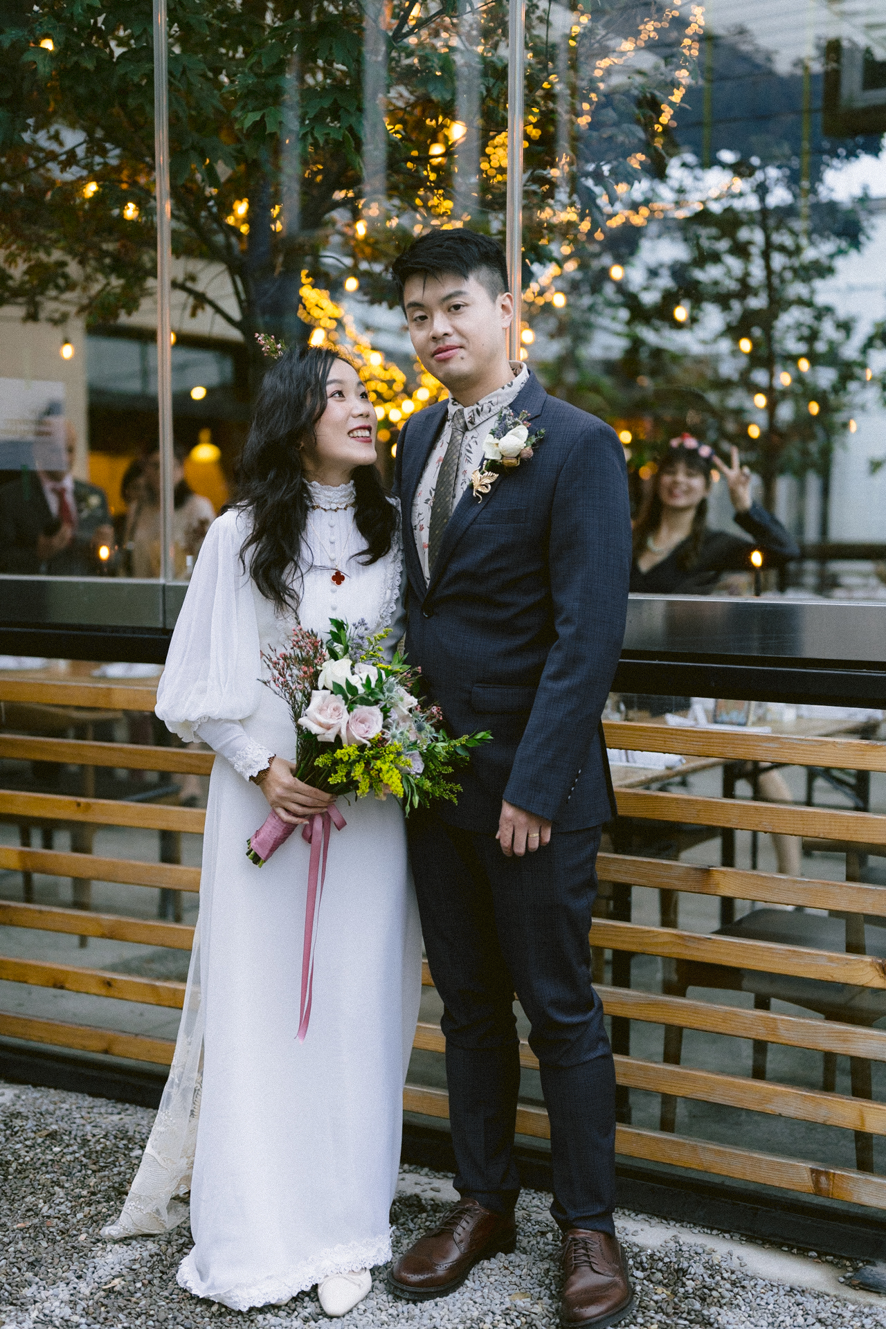 A couple in wedding attire posing for a photo with twinkle lights in the background.