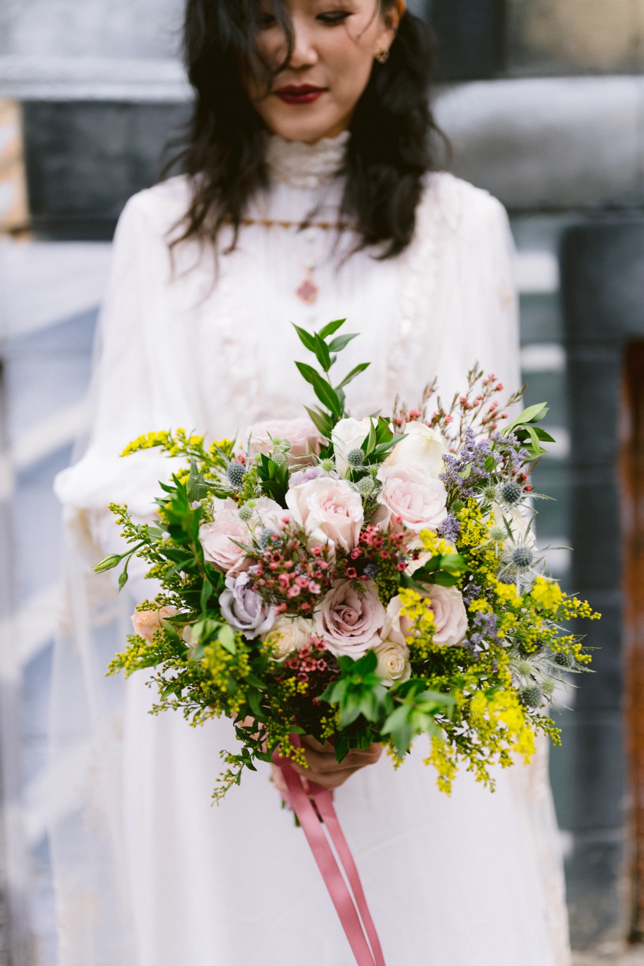 A bride in a white dress holding a bouquet stands in front of a graffiti wall for her micro-wedding