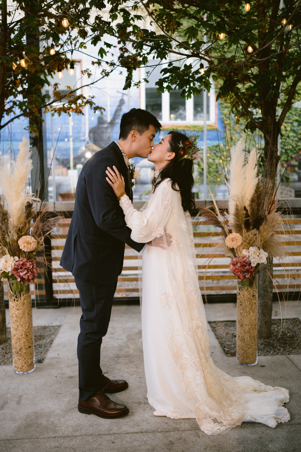 A couple kissing during their wedding ceremony under a canopy of lights.