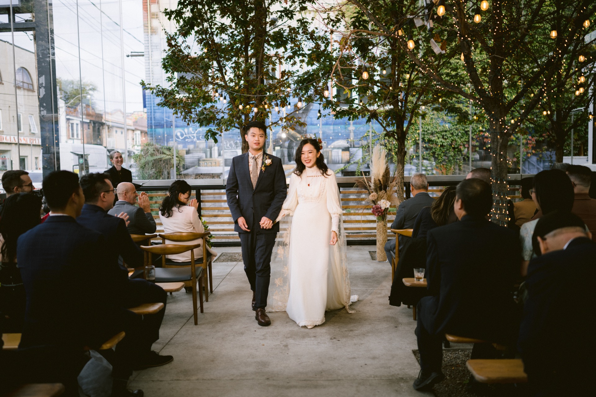 A bride and groom walking down the aisle at an outdoor wedding ceremony with guests seated on either side.