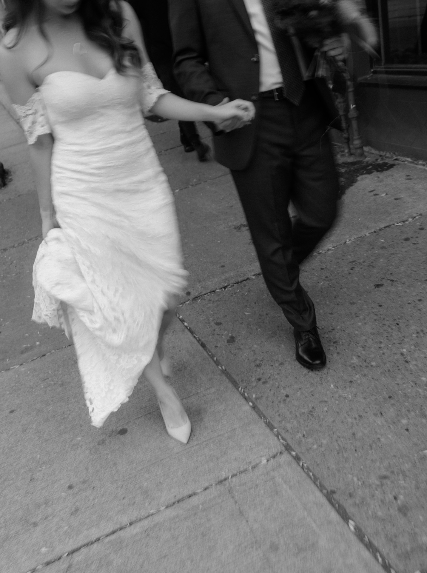 Bride and groom holding hands on a city street while heading to their wedding venue.
