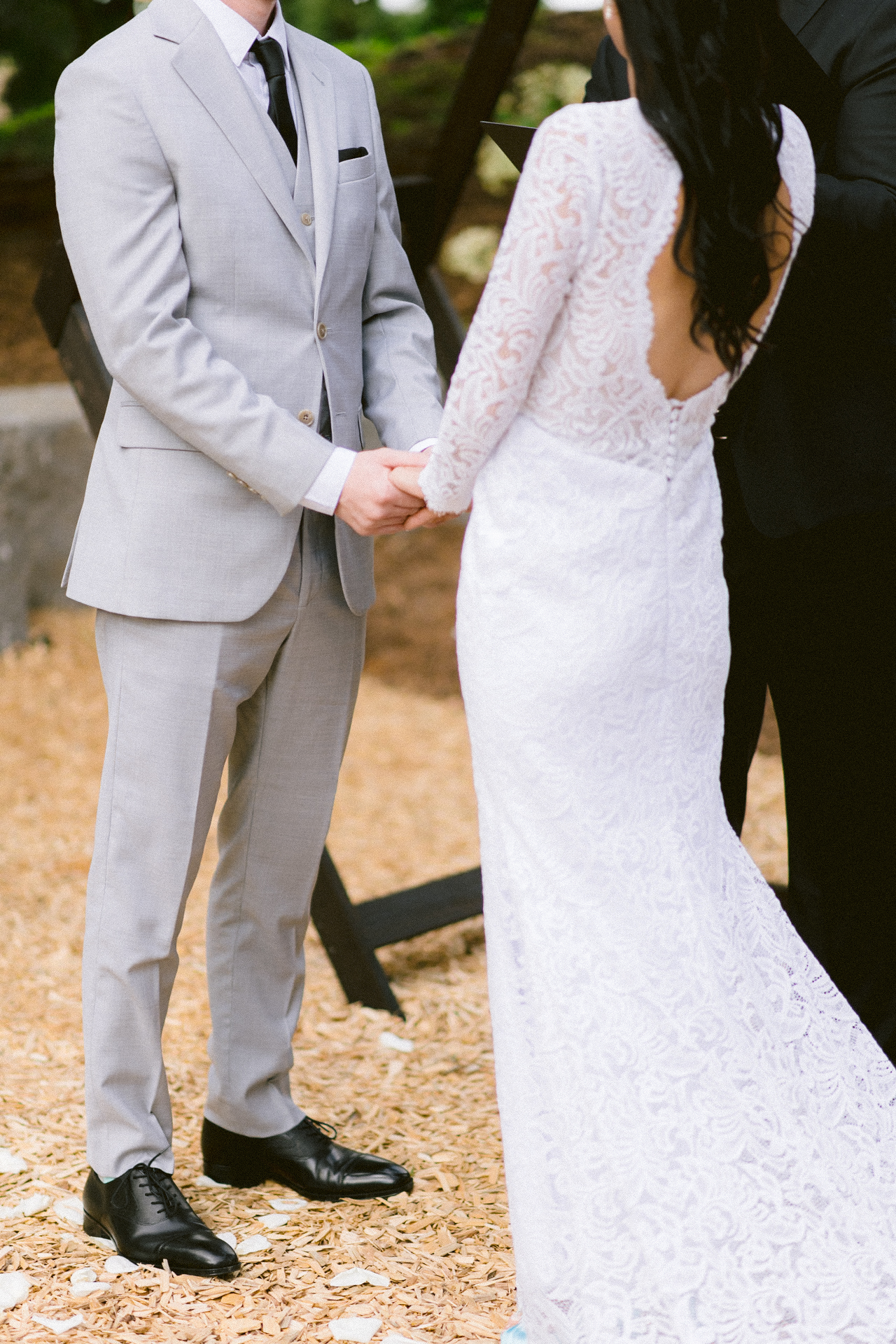 Bride and groom holding hands on their wedding day, with the focus on their interlocked hands and wedding attire.
