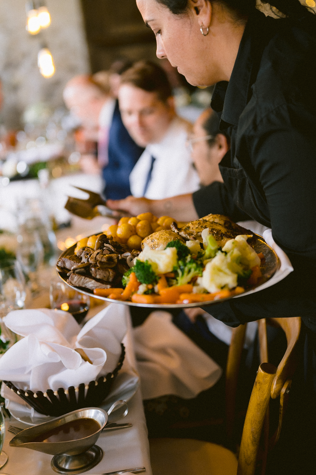 Waitress serving a platter of roast chicken and vegetables at a dining event.
