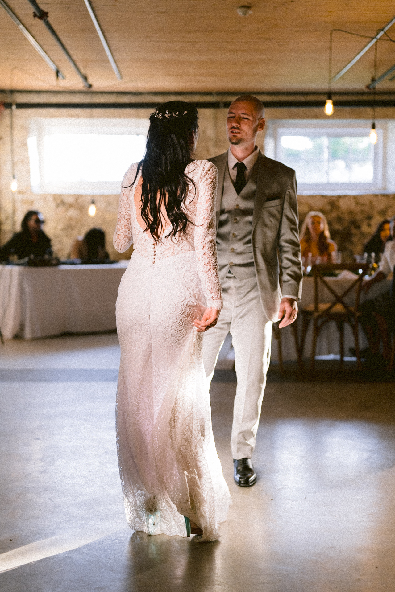 A couple sharing a dance in a warmly lit venue, with guests seated in the background