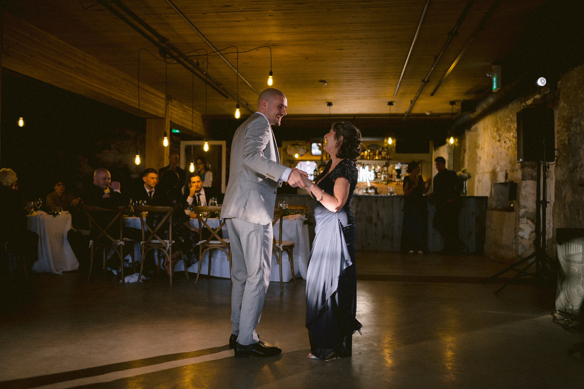 Groom dance joyfully with his mother during the parent dance session when the Toronto wedding photographer capture the expression of guests as background.