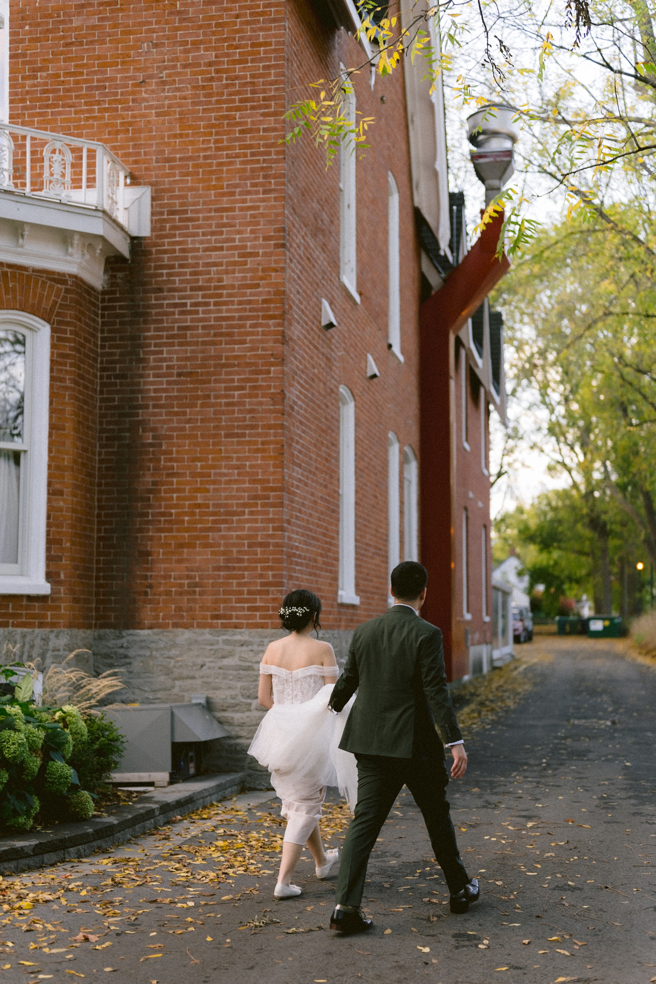 A couple in wedding attire holding hands in front of a victorian-style house