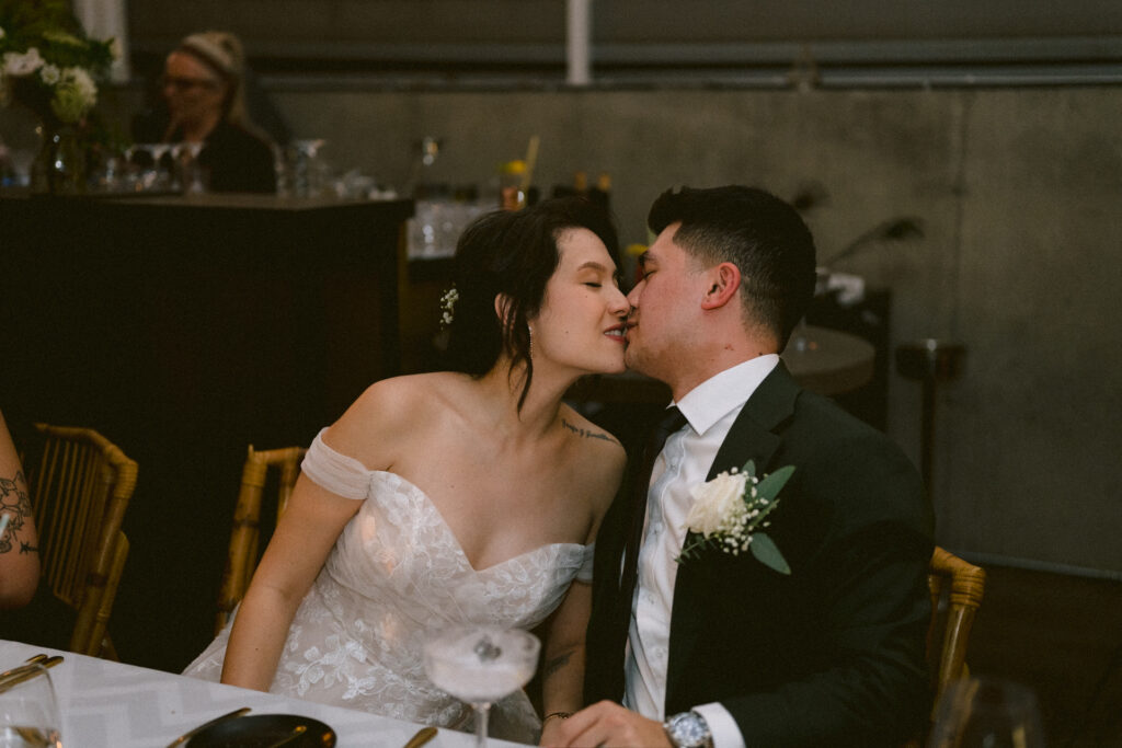 A bride in a white dress and a man in a suit embracing during an indoor wedding ceremony.