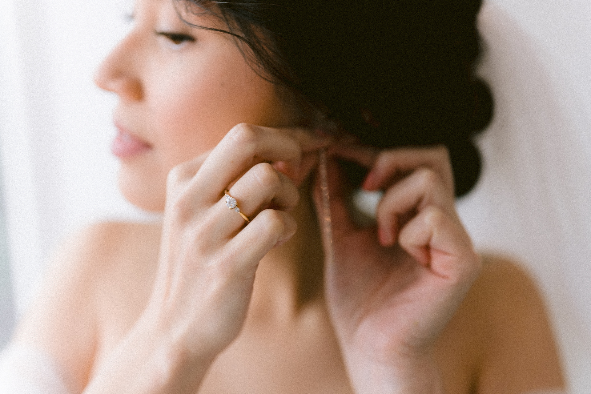 Bride looking out the window while adjusting her earrings.