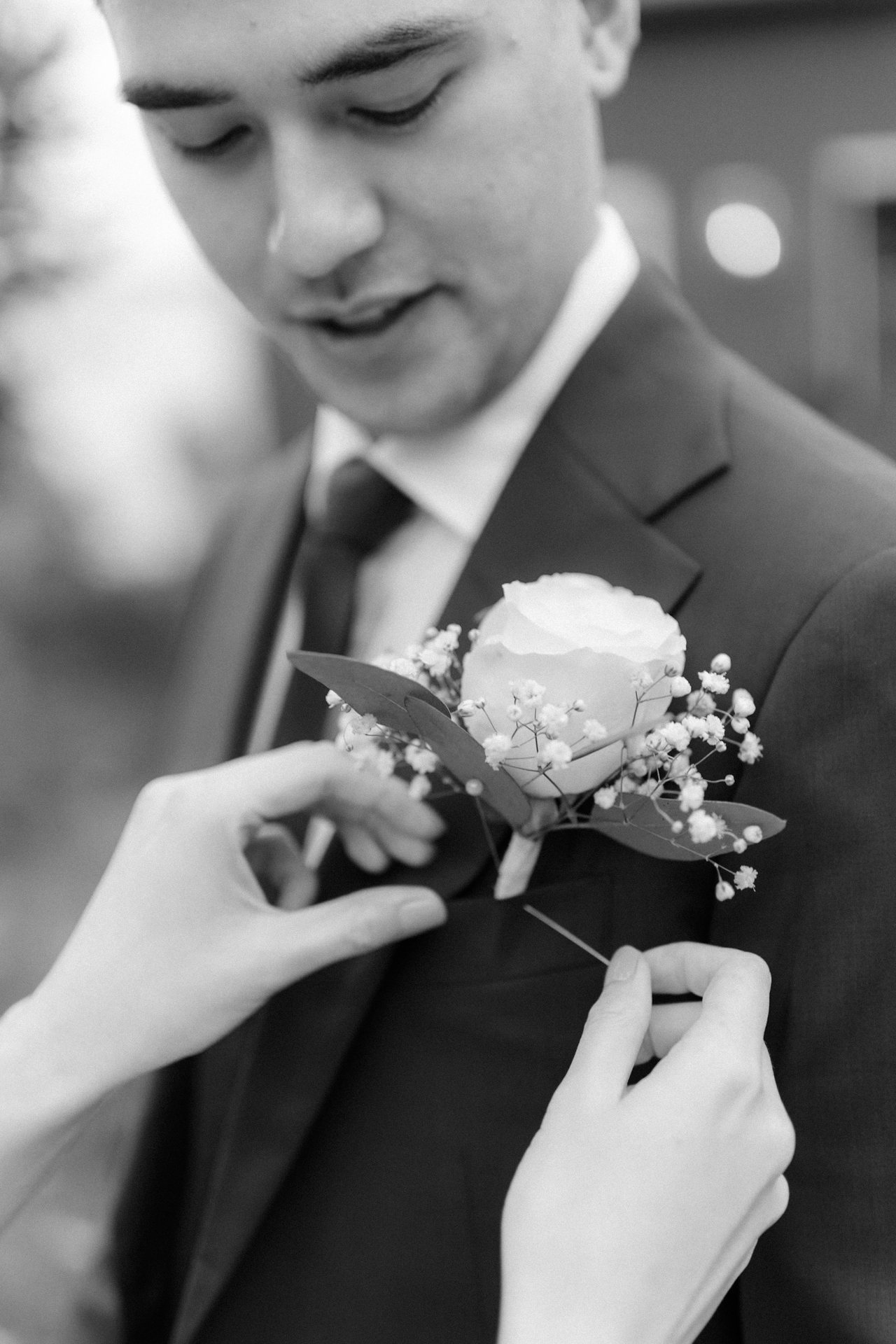 A man in a suit adjusting a white boutonnière.