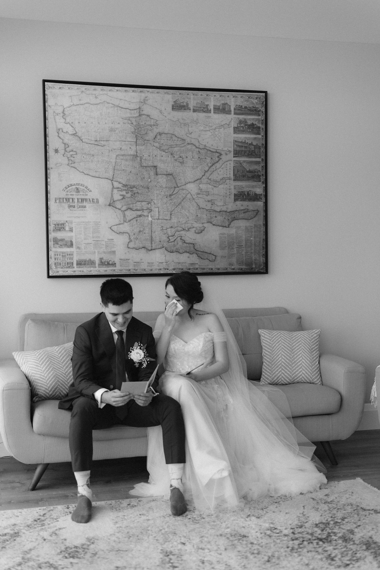 A bride and groom sitting on a sofa, reading heartfelt notes, with the groom appearing to wipe a tear and the bride smiling