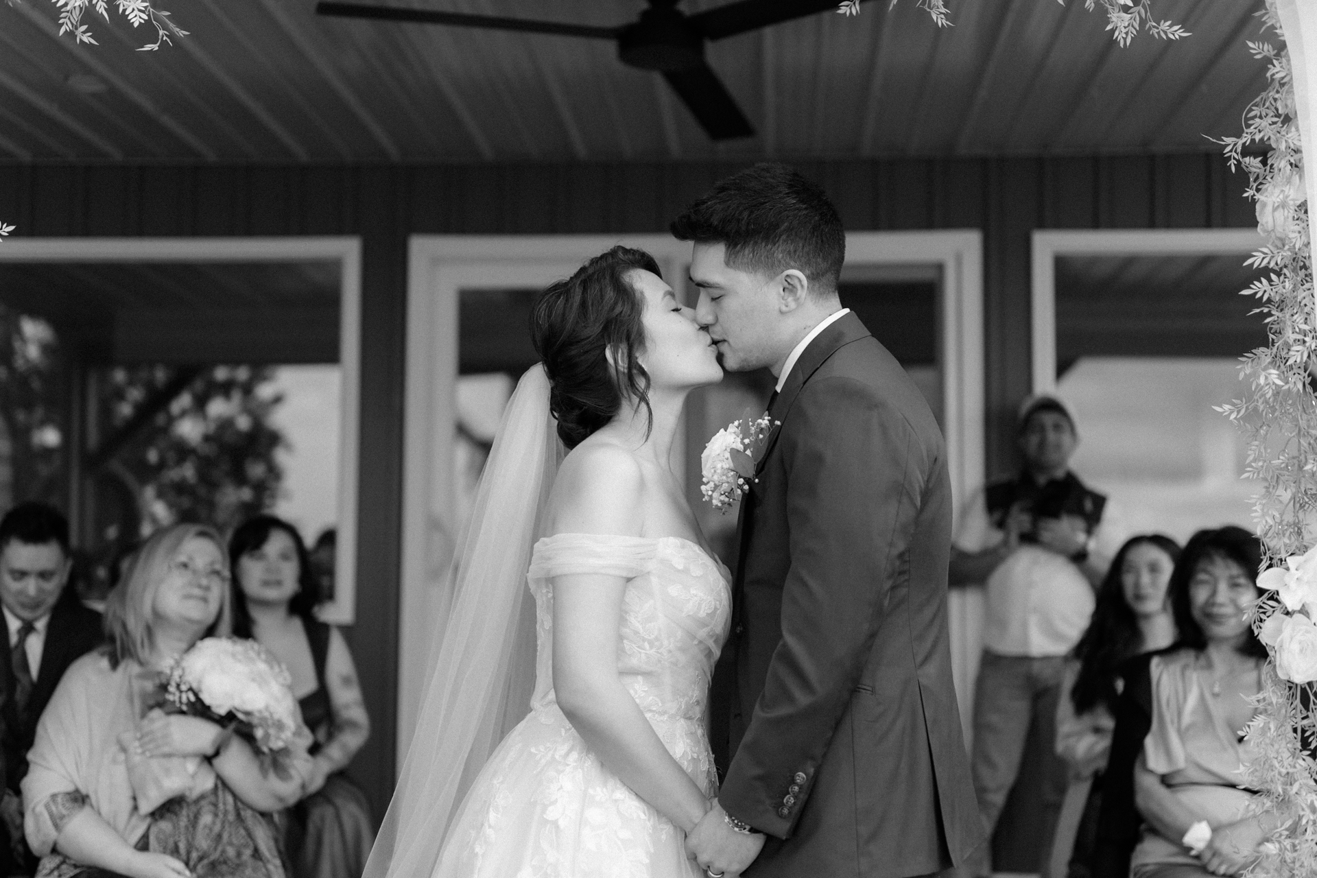 A bride and groom sharing a kiss at their wedding ceremony while guests look on
