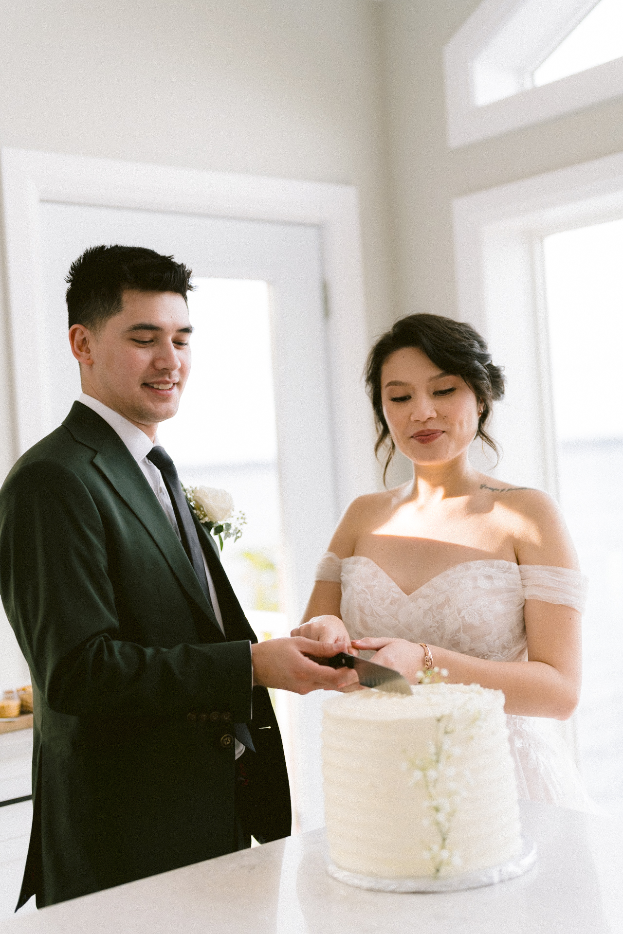 A bride and groom cutting a white wedding cake adorned with small flowers