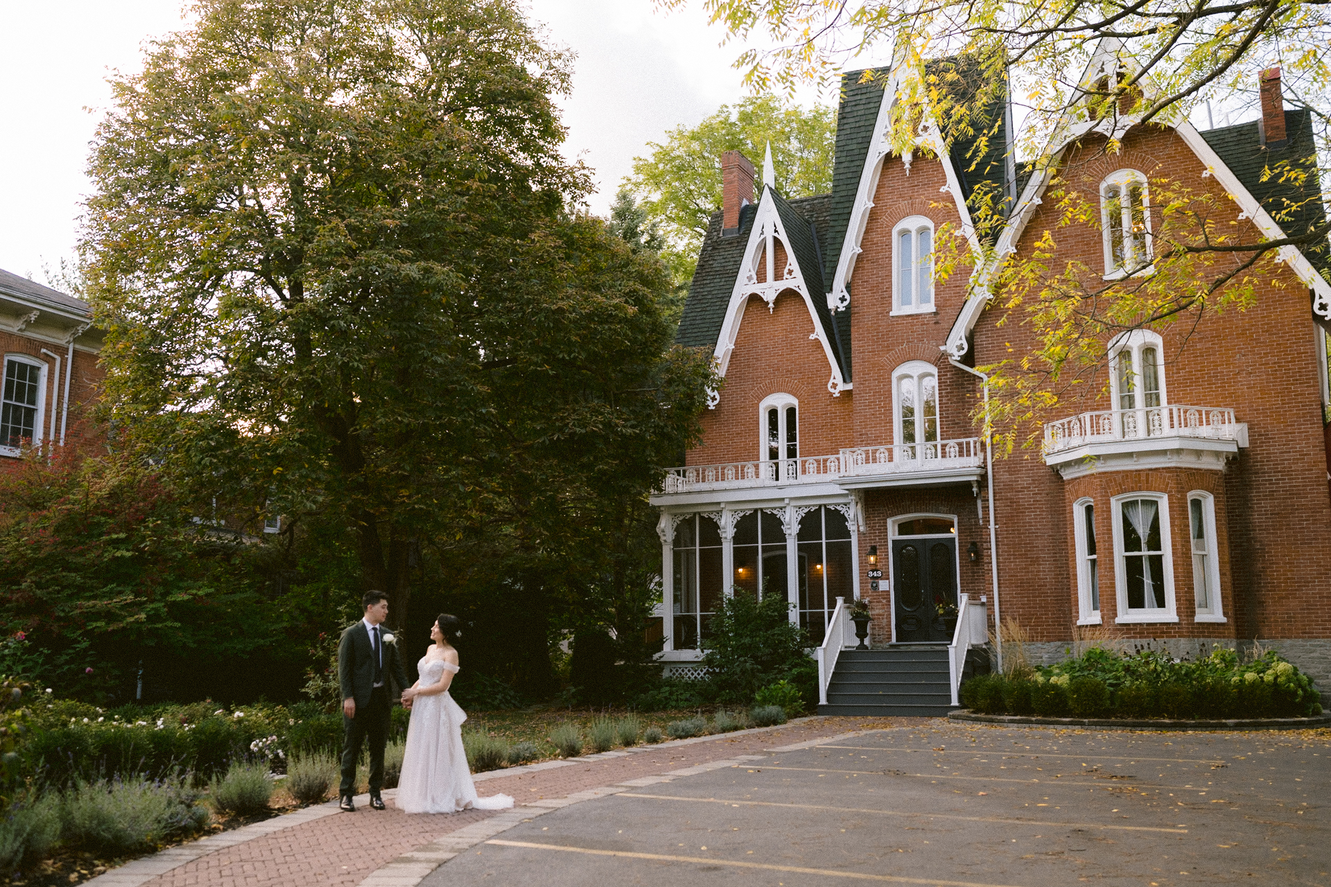 A couple in wedding attire holding hands in front of a victorian-style house at Merrill House.