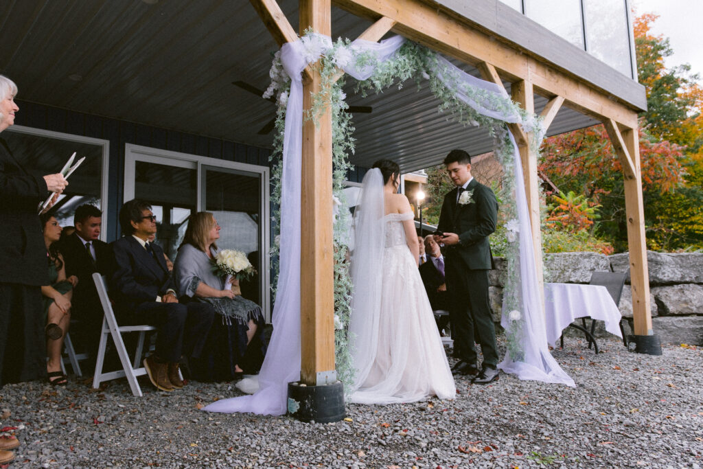 A couple exchanges vows at an outdoor wedding ceremony with guests looking on