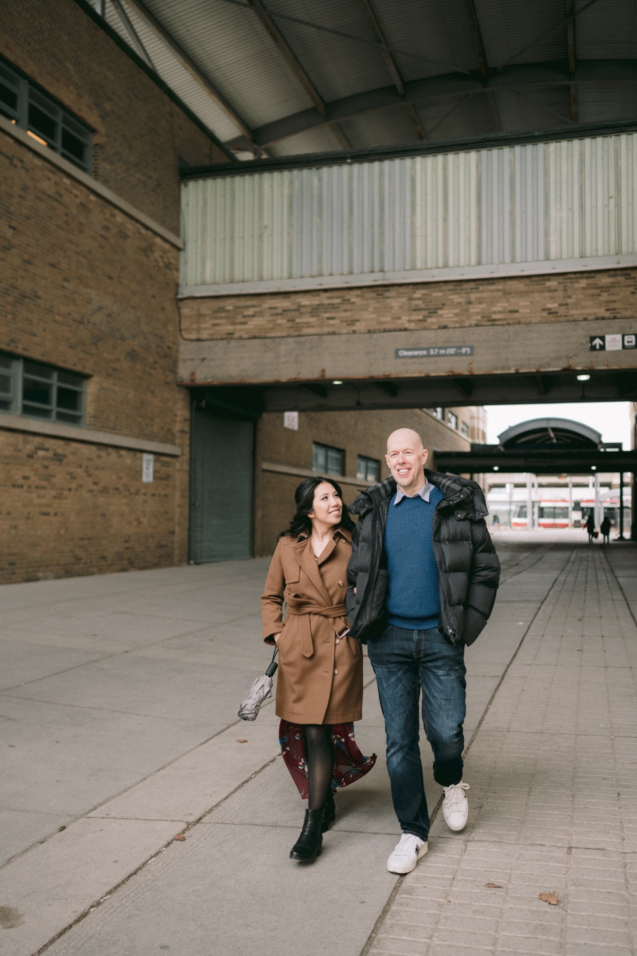 A couple walking together and smiling outside a brick building with an industrial look during their engagement session