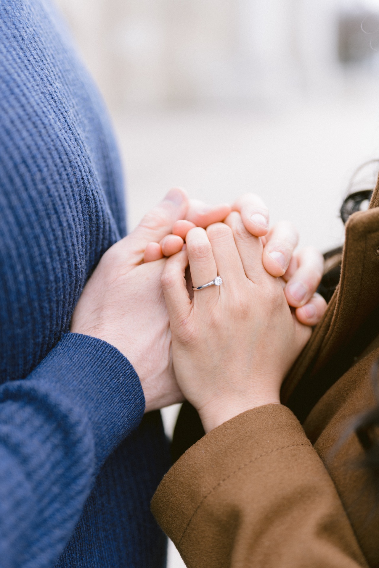 A couple showcasing engagement rings while standing close to each other with a blurred background.