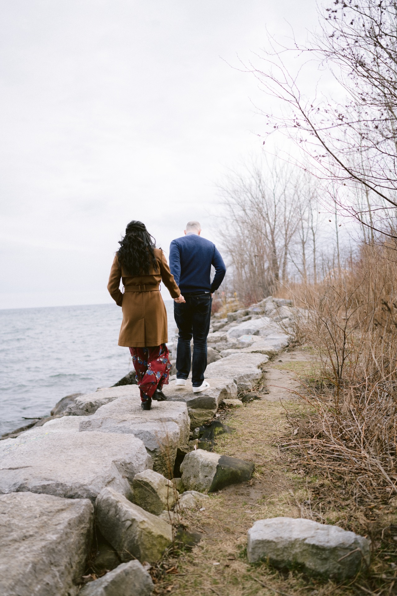 Two people walking along a rocky shoreline.