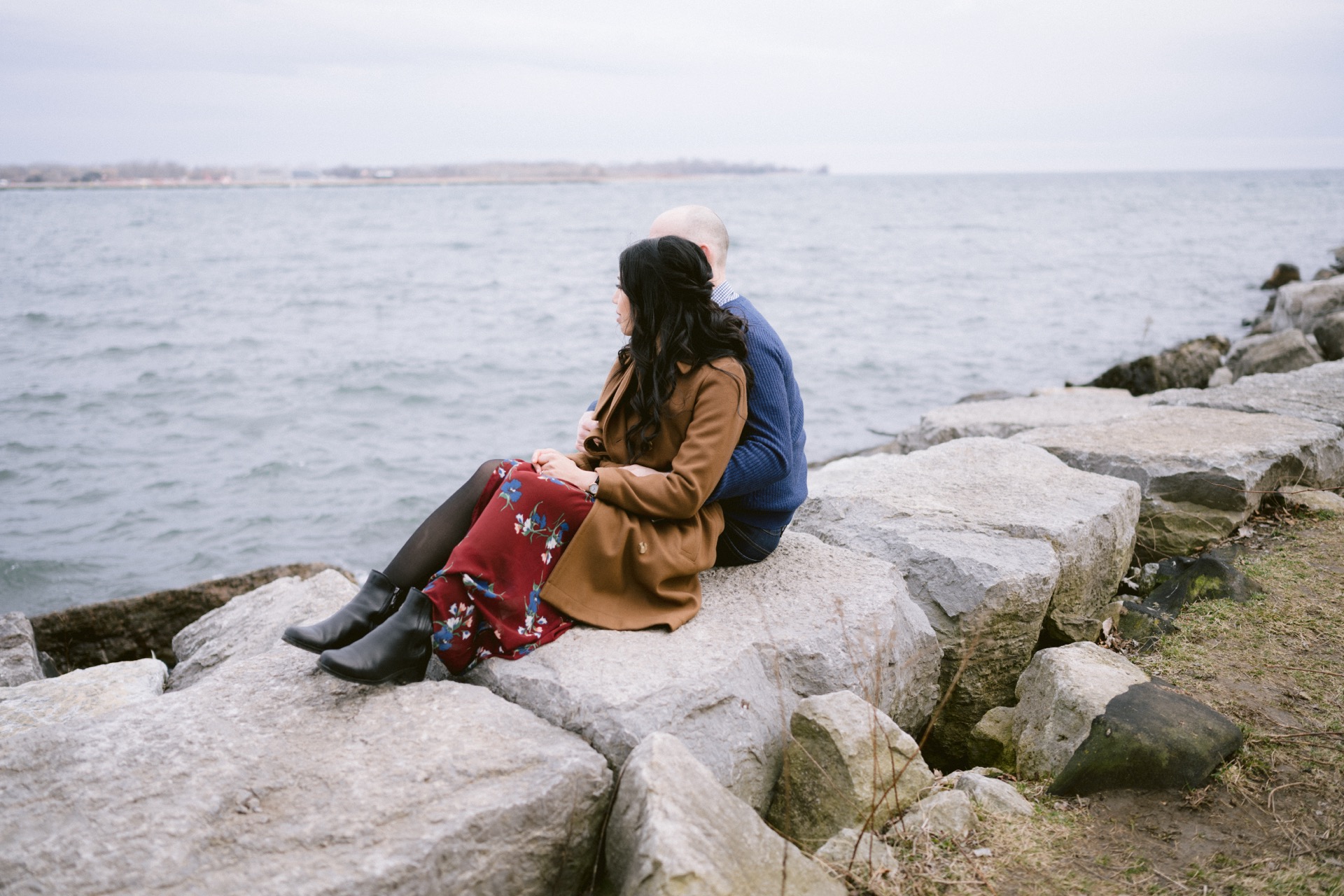 Two individuals sitting on rocky shore overlooking the water