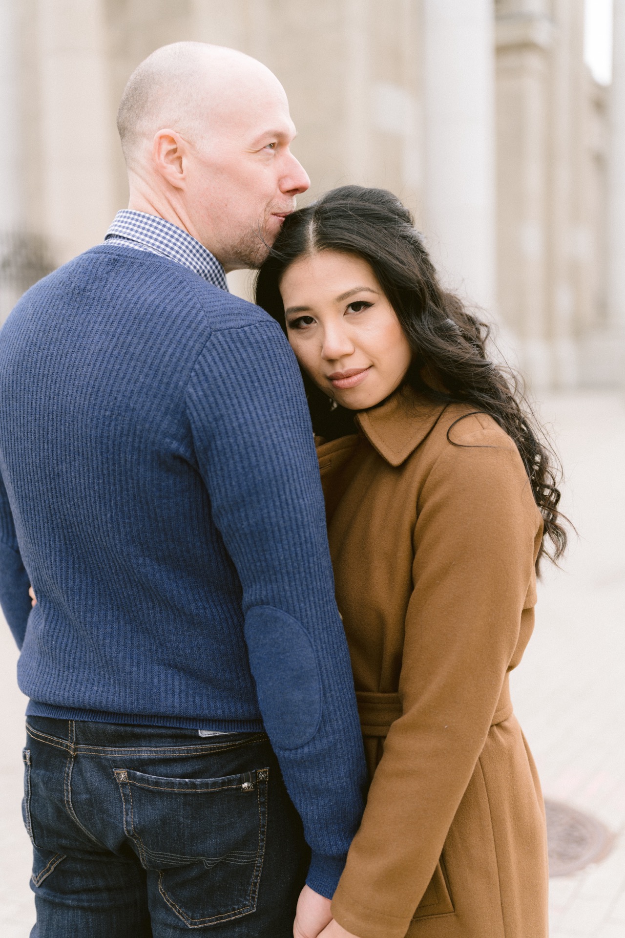 A couple embracing, with the man kissing the woman's forehead as they pose for a photo.