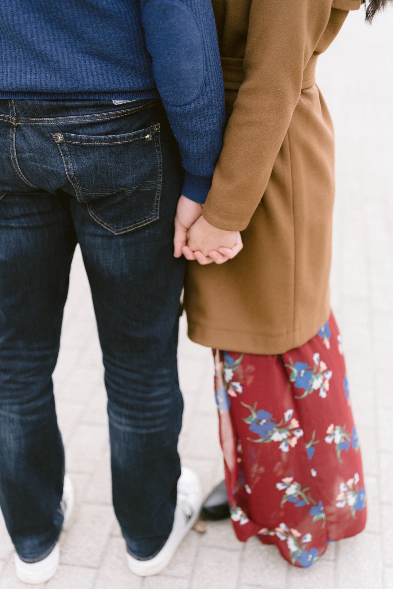 A couple holding hands behind their backs, each wearing one casual and one smart outfit element.