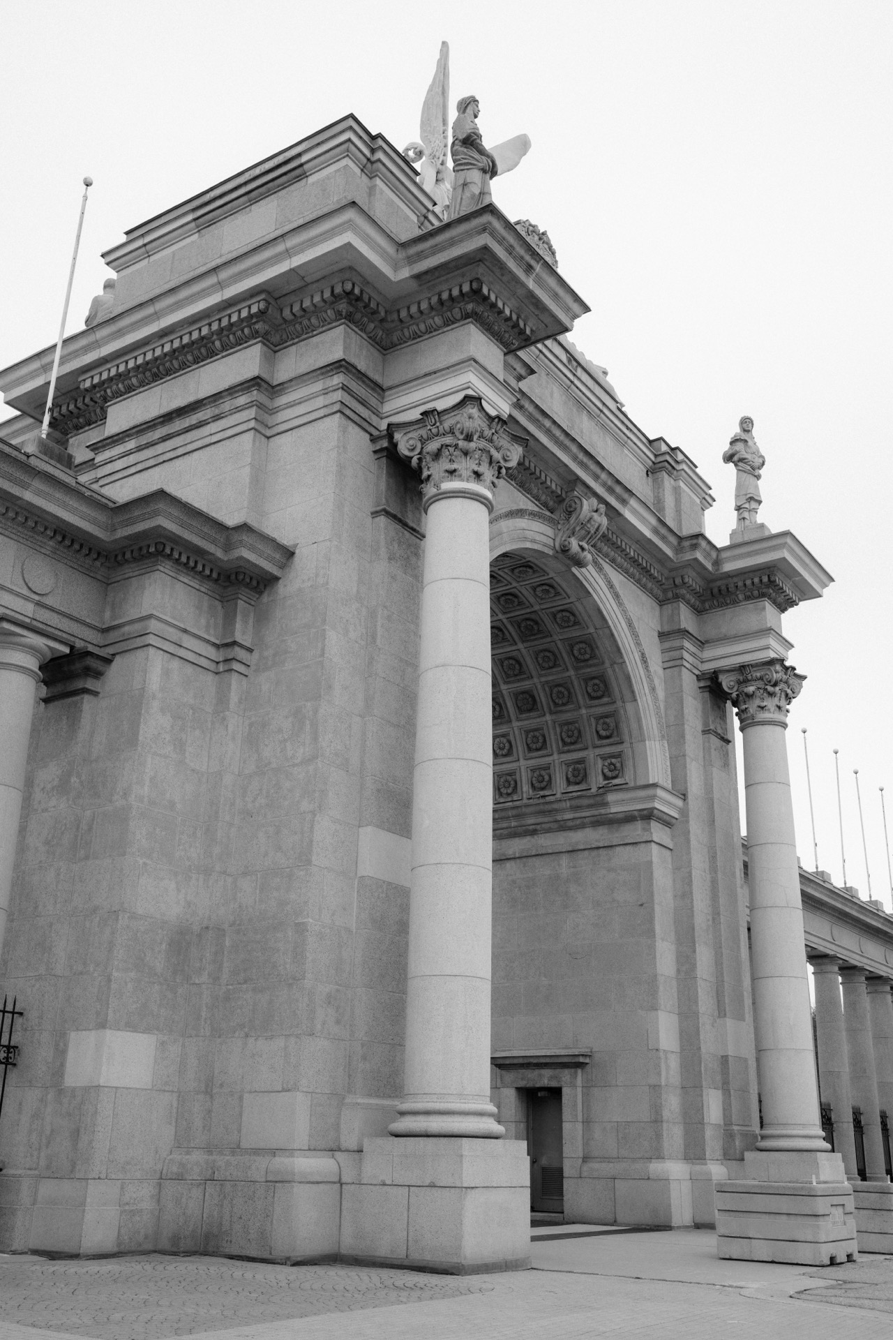 An angled view of a neoclassical building facade with columns and a statue on top.