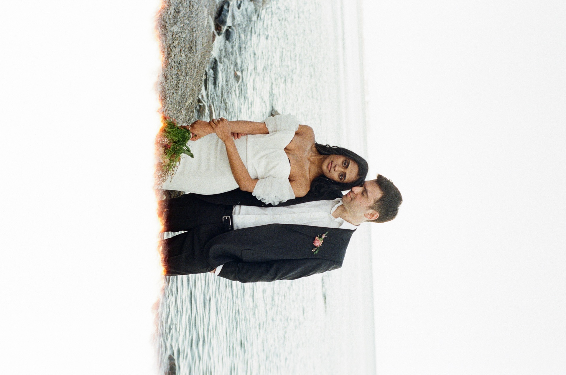 Couple poses for their wedding portrait by a lake with a film camera.