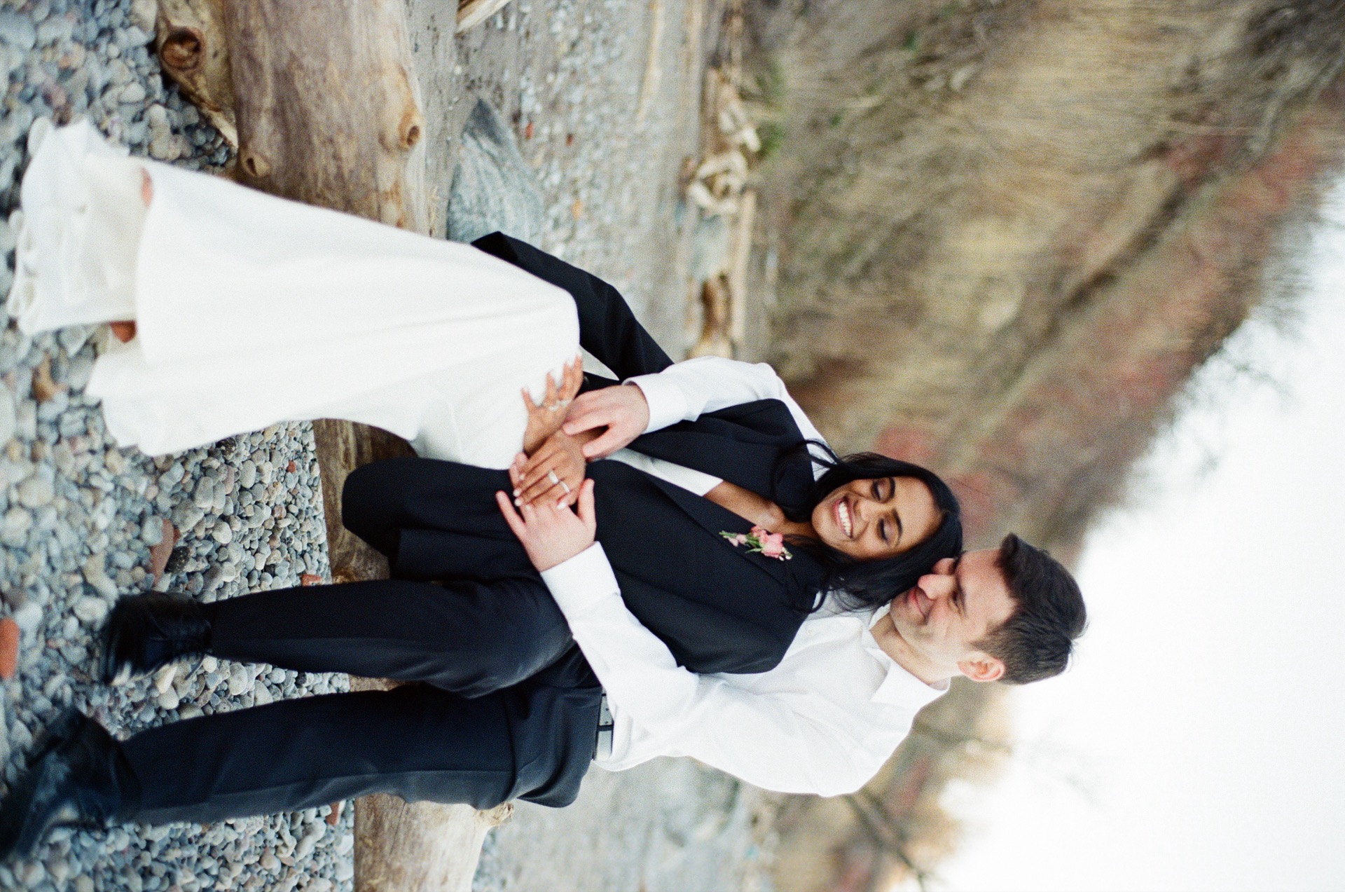 A newlyweds sit on a log and cuddle together after their wedding ceremony by Lake Ontario.