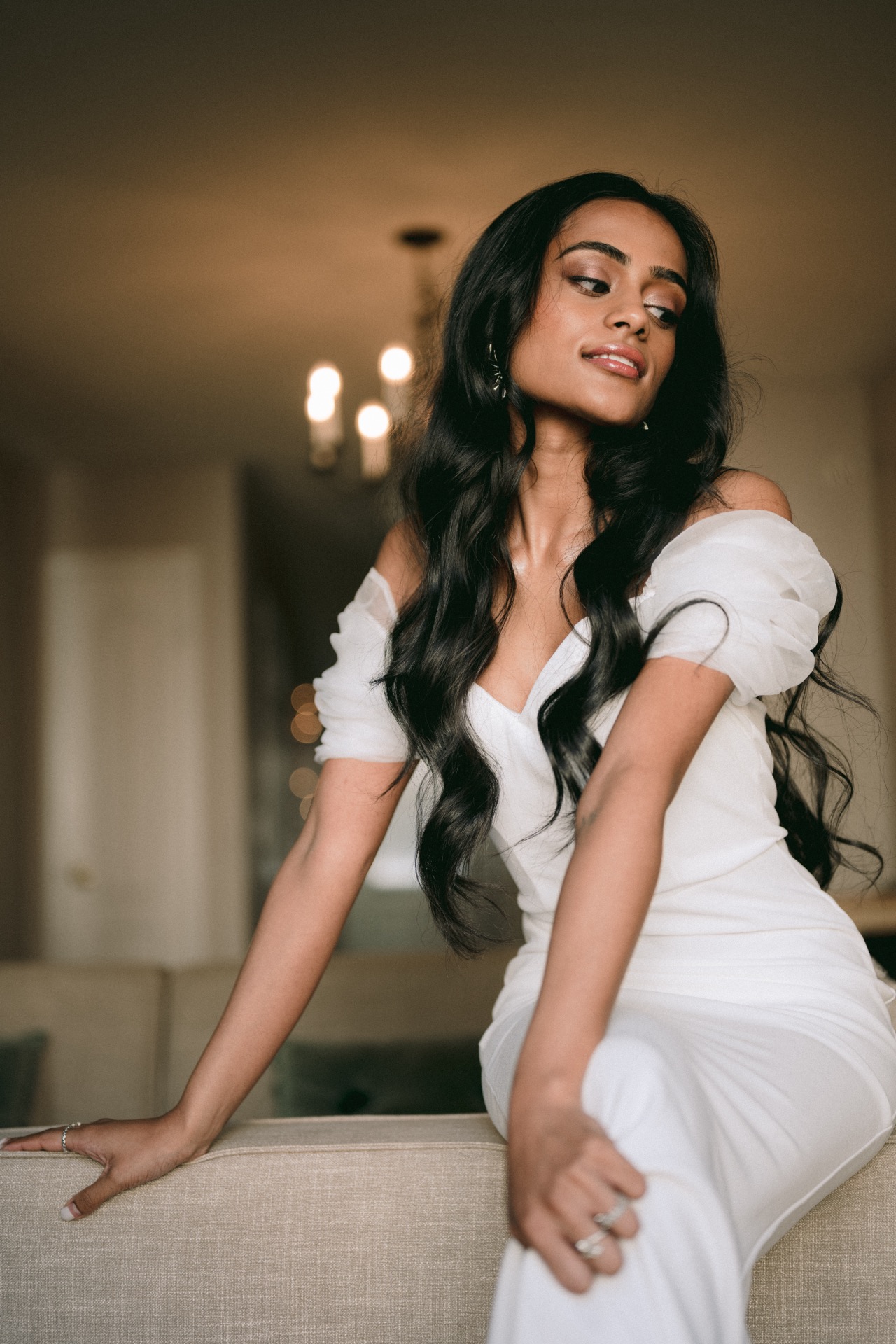 A bride sit elegantly on a sofa when she is getting ready for her wedding.