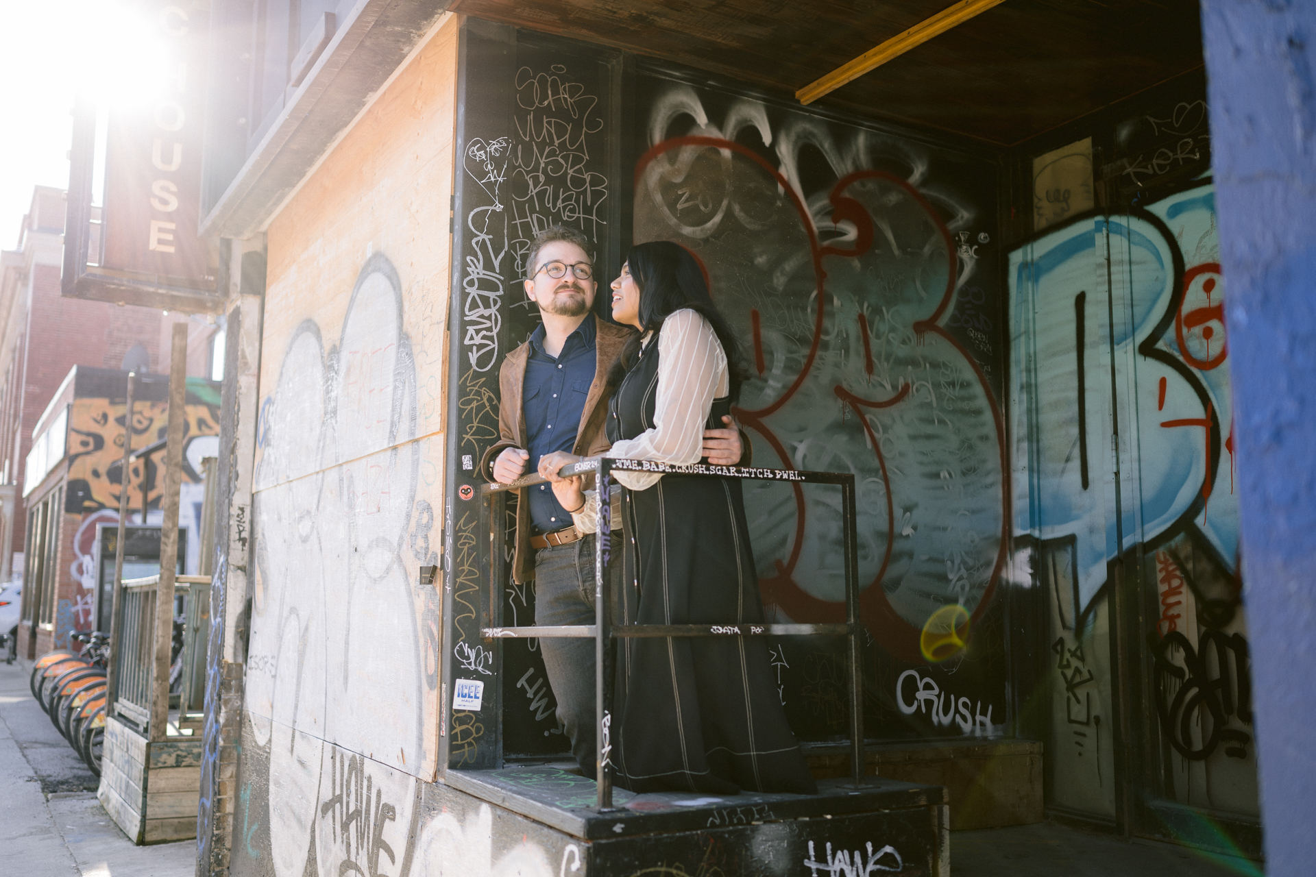 A man hugging his girlfriend tightly at an abandon shop with full of murals.