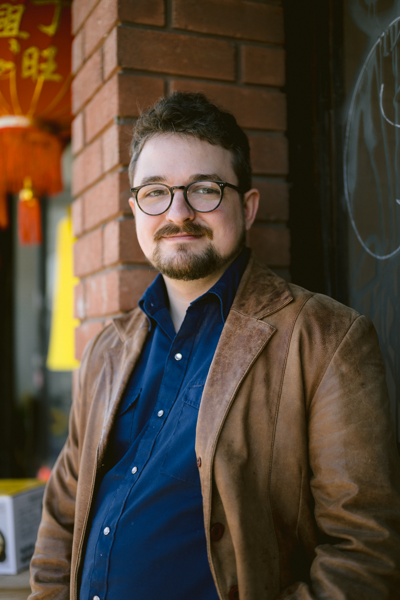 A man in his brown jacket poses poses at Gerrard Street for his couple shoot with an engagement photographer Toronto.