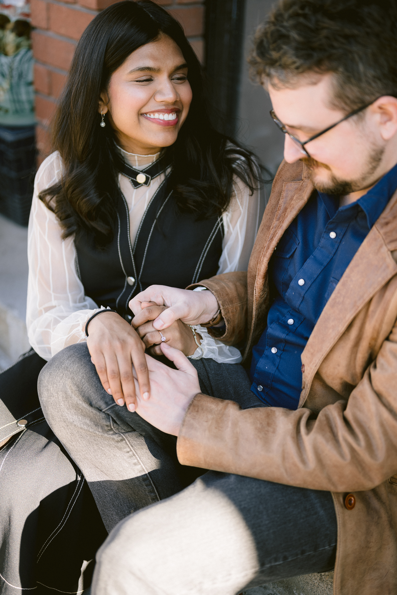 A man holding his girlfriend's hand and looking closely on her engagement ring.