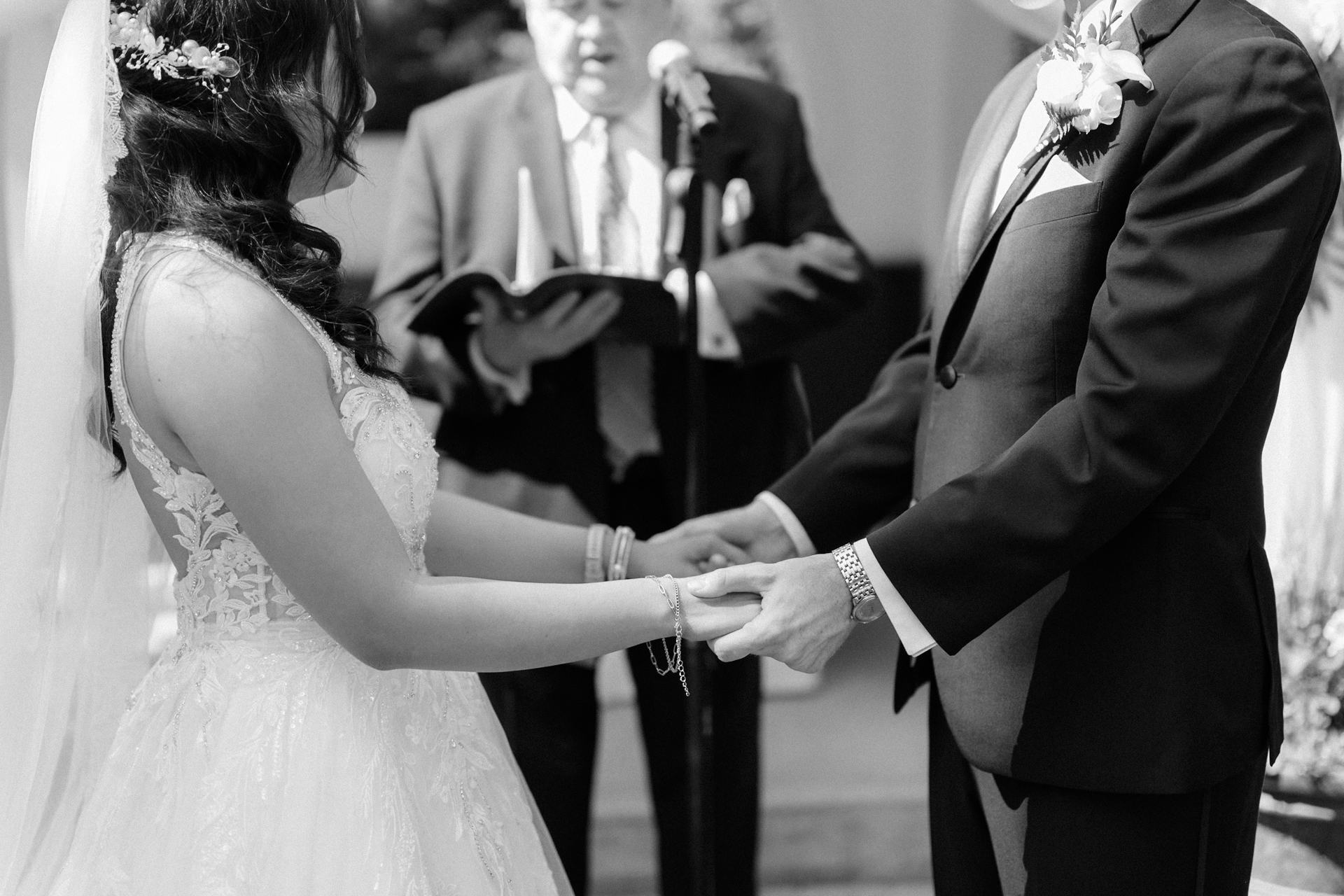 A couple holding hands during their wedding ceremony with an officiant in the background.
