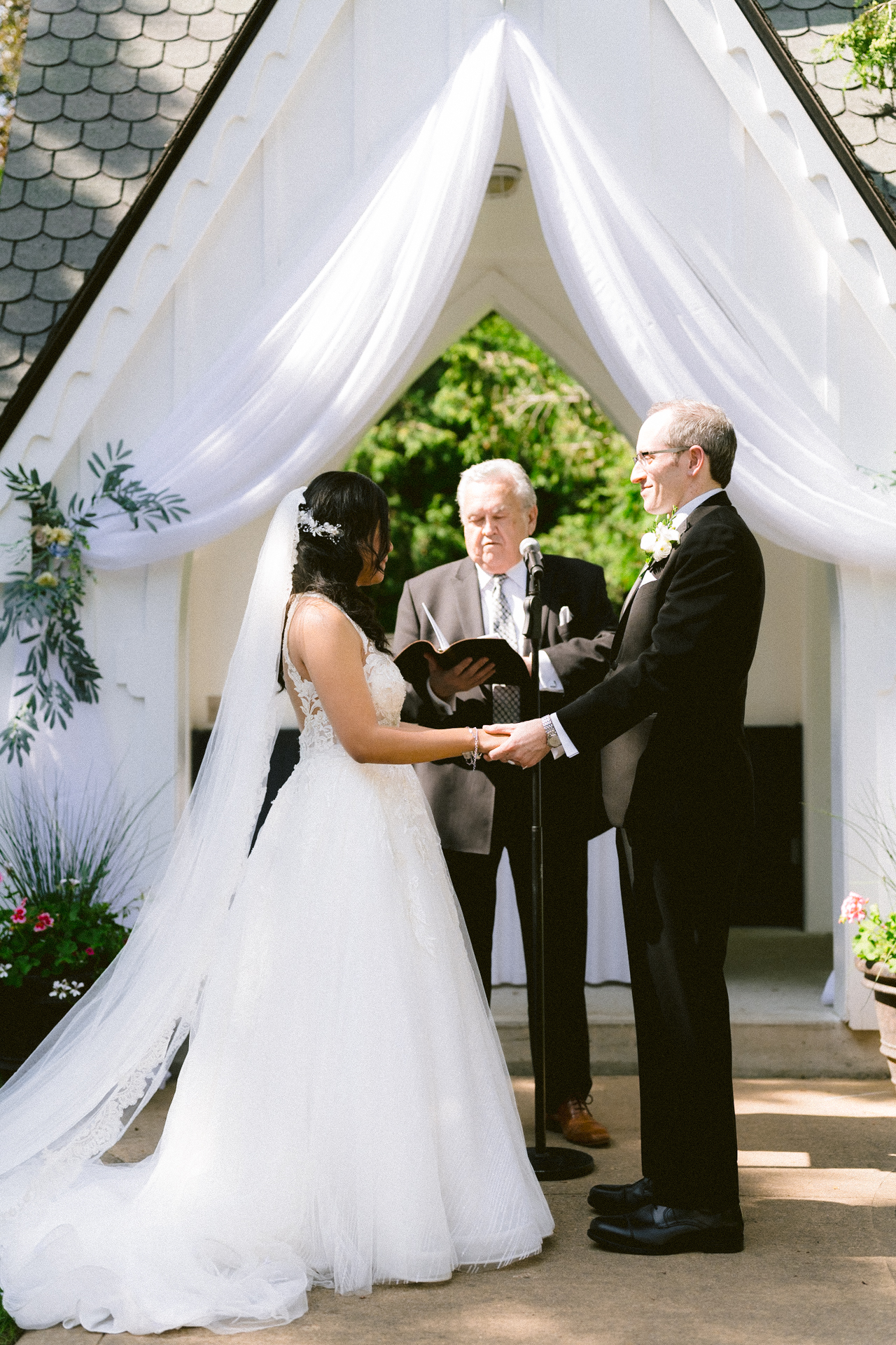 A bride and groom exchanging vows at an outdoor wedding ceremony with an officiant presiding.