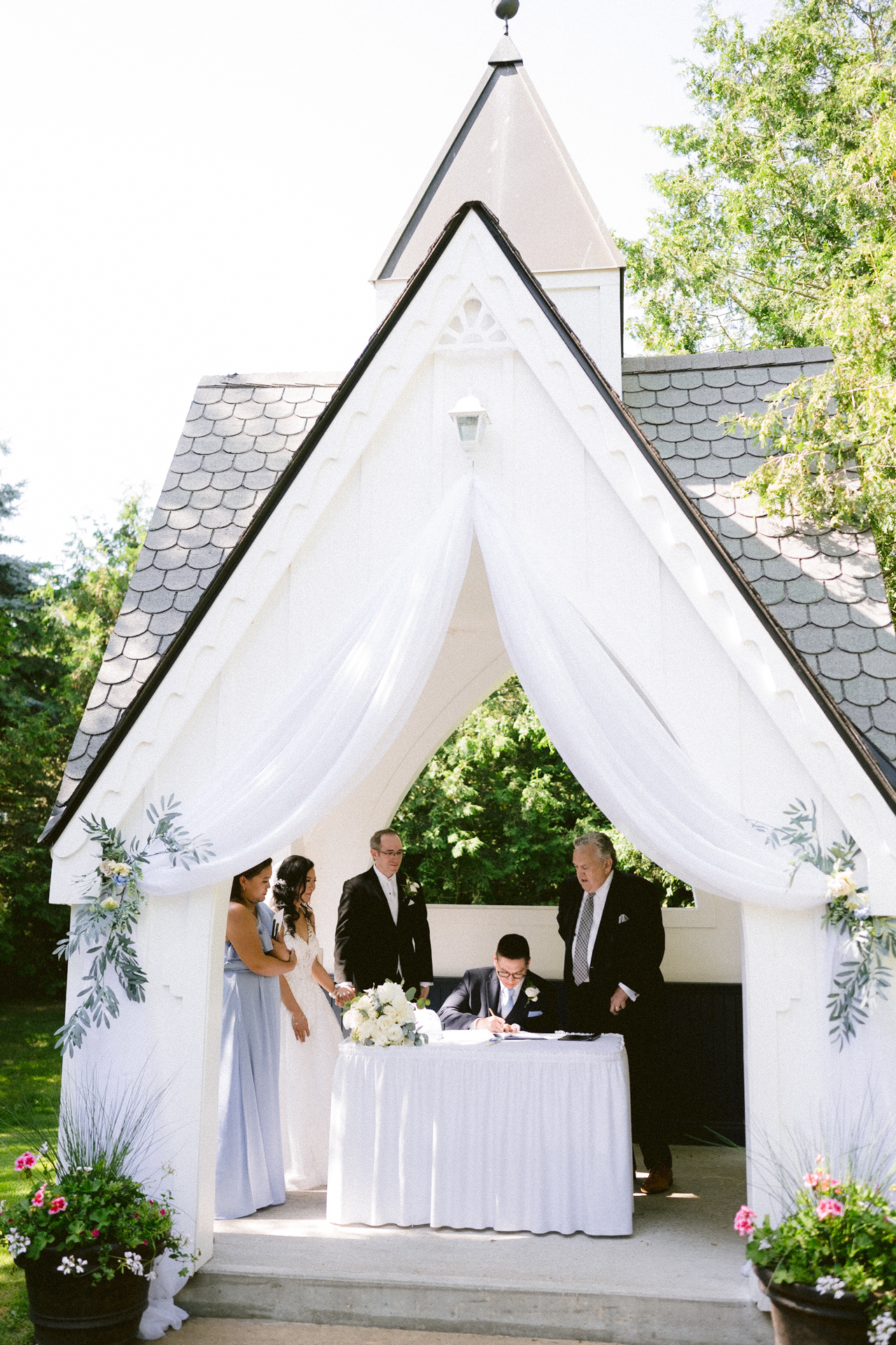 A wedding ceremony taking place under a white gazebo with the officiant and a couple at the altar.