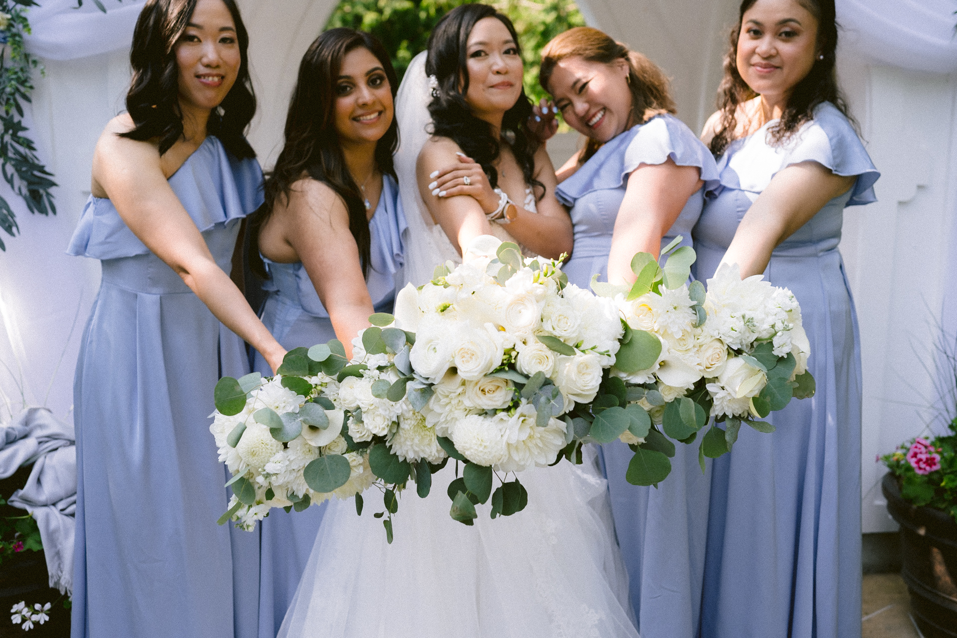 A bride and her bridesmaids in blue dresses holding bouquets of white flowers.