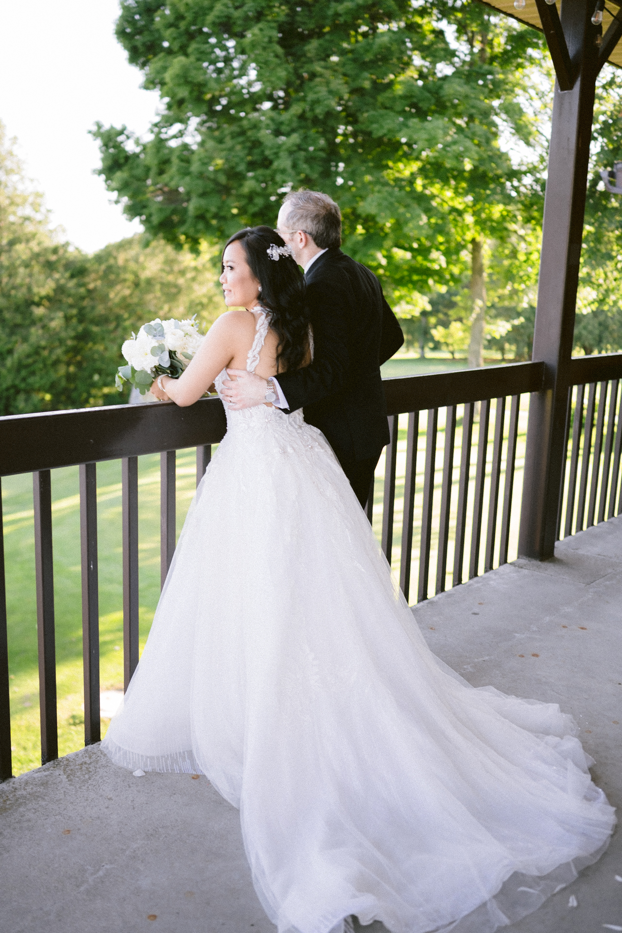 A bride and groom standing together on a balcony, surrounded by greenery.