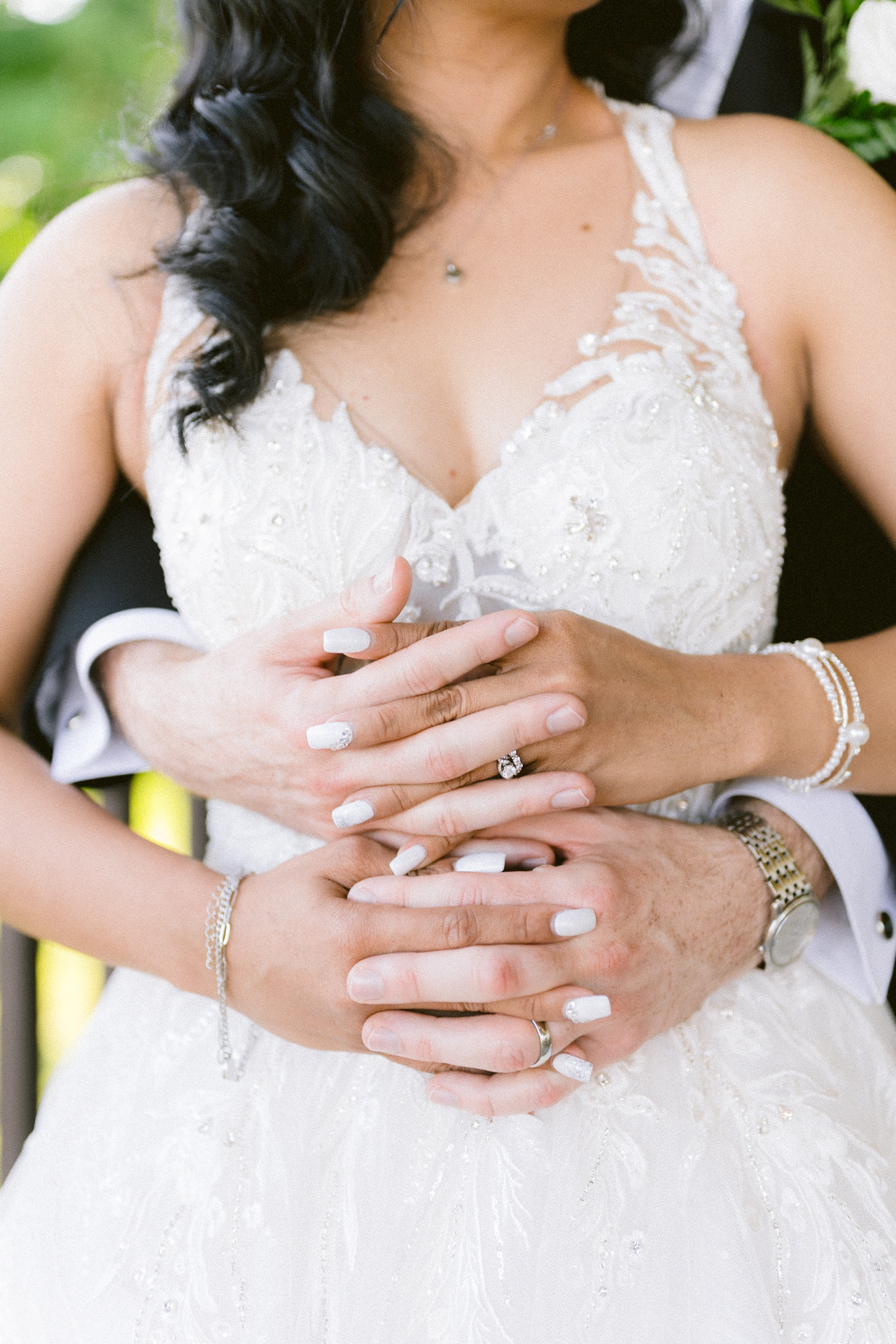 A close-up of a bride and groom hands clasped together, showcasing wedding attire and rings.