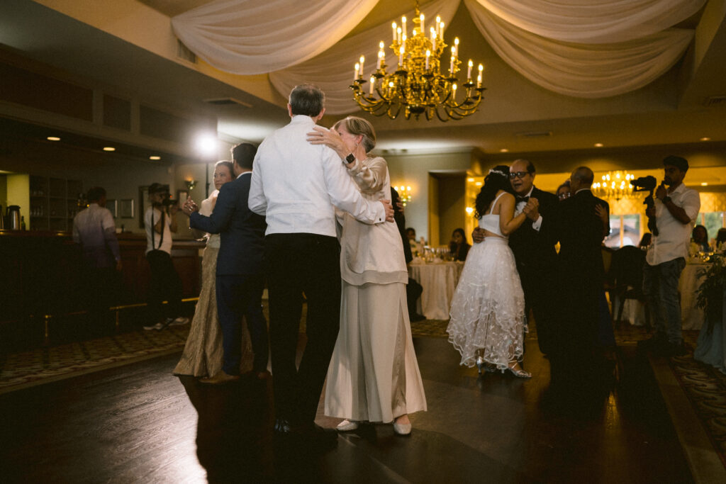 A couple dances together in an elegant ballroom with onlookers seated in the background.