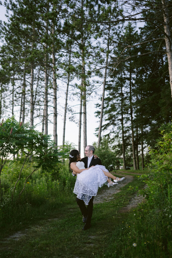 Groom carrying bride in a forested area.