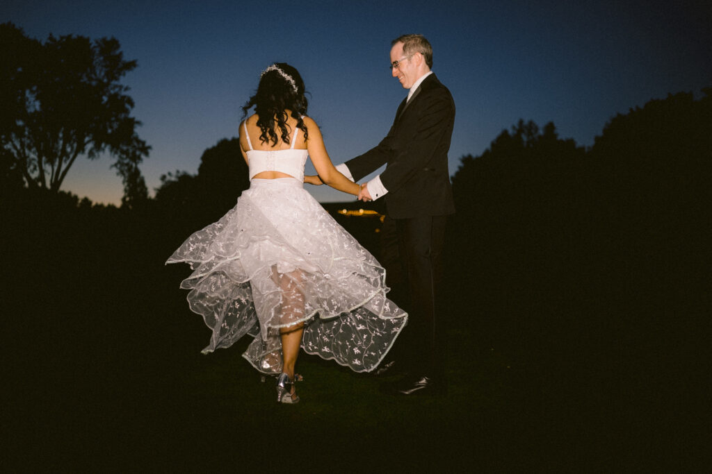 A bride and groom walking together and smiling in a twilight outdoor setting.