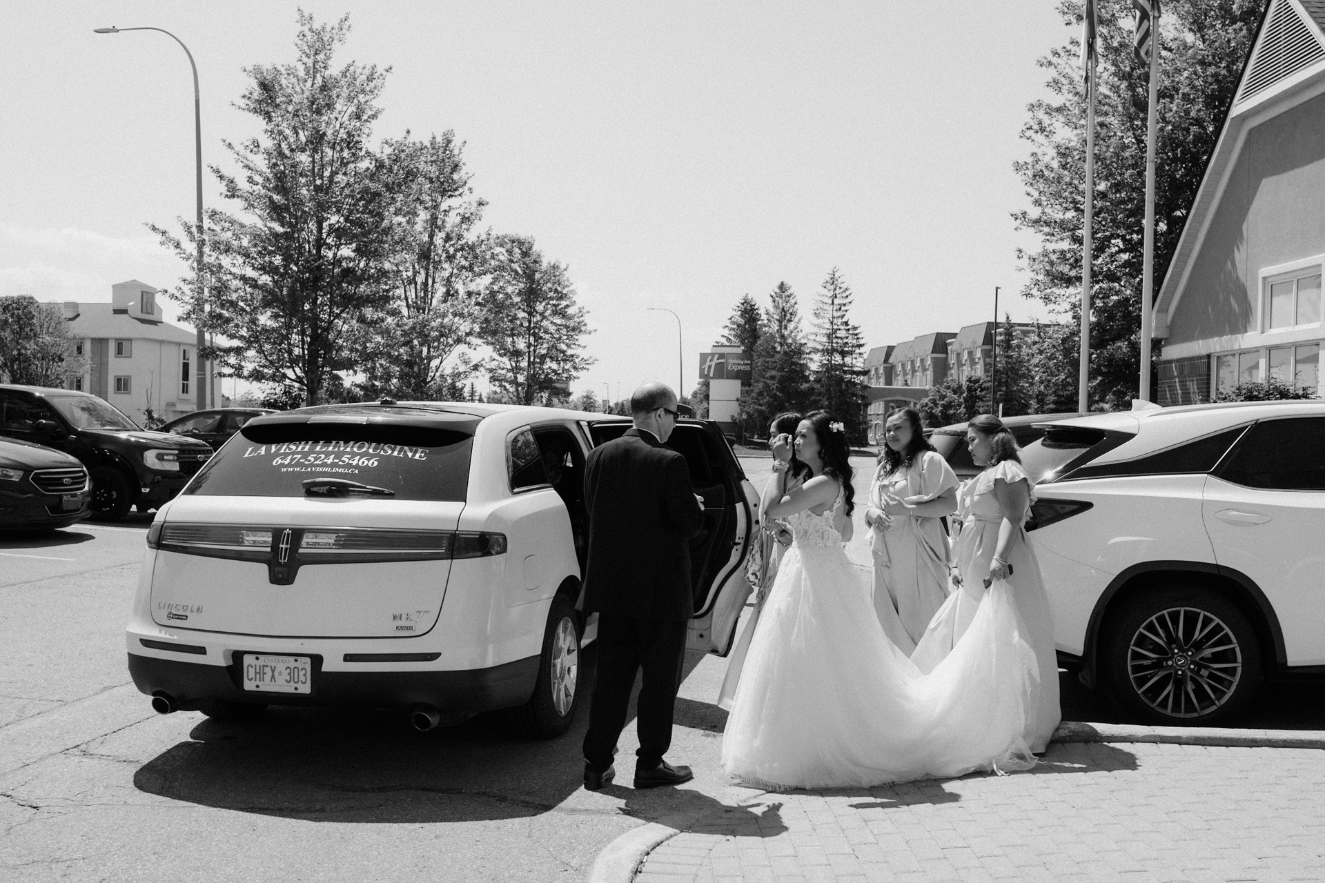 A bride stepping out of a limousine with assistance, accompanied by bridesmaids.