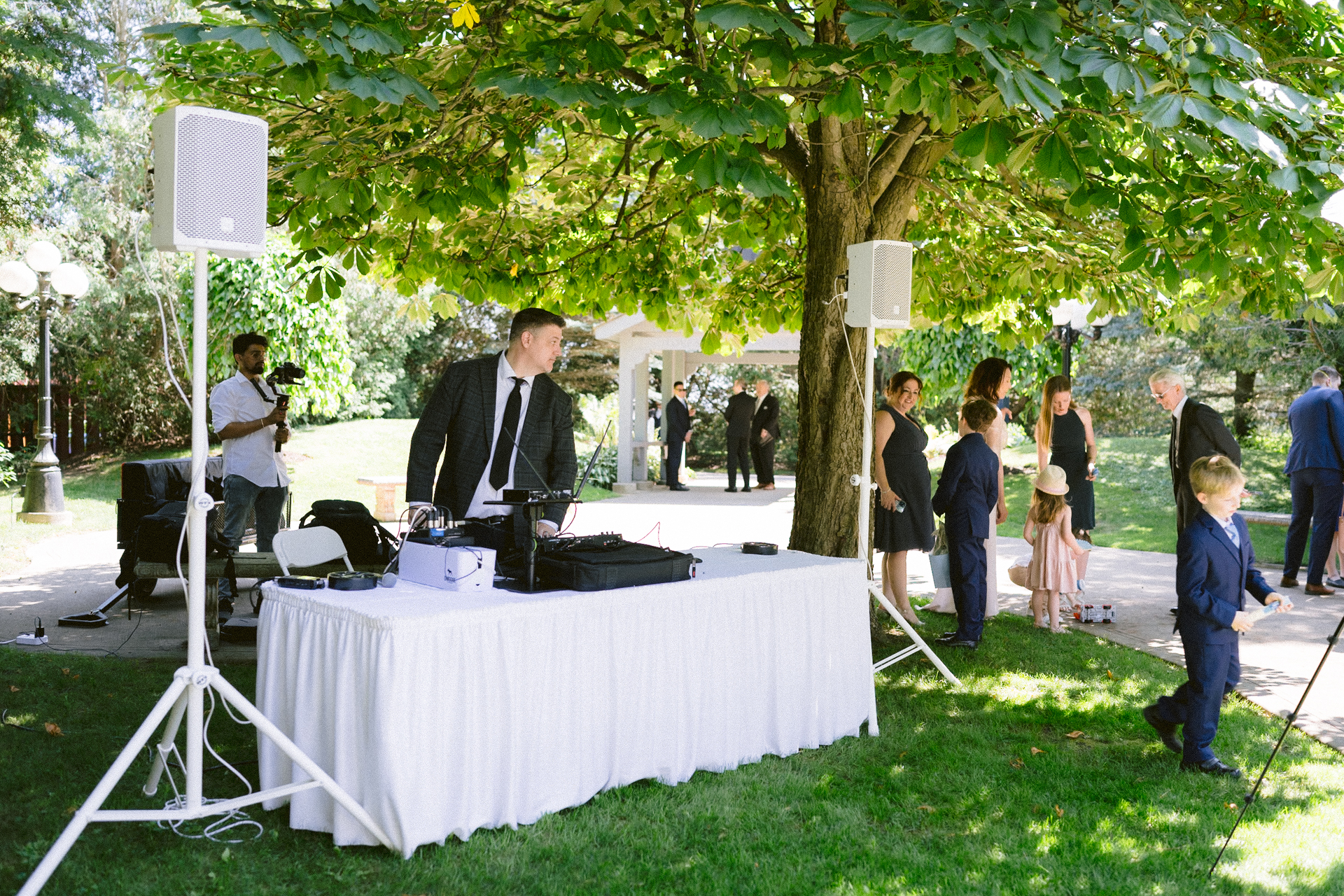 Outdoor event with guests and a dj setup under a tree.