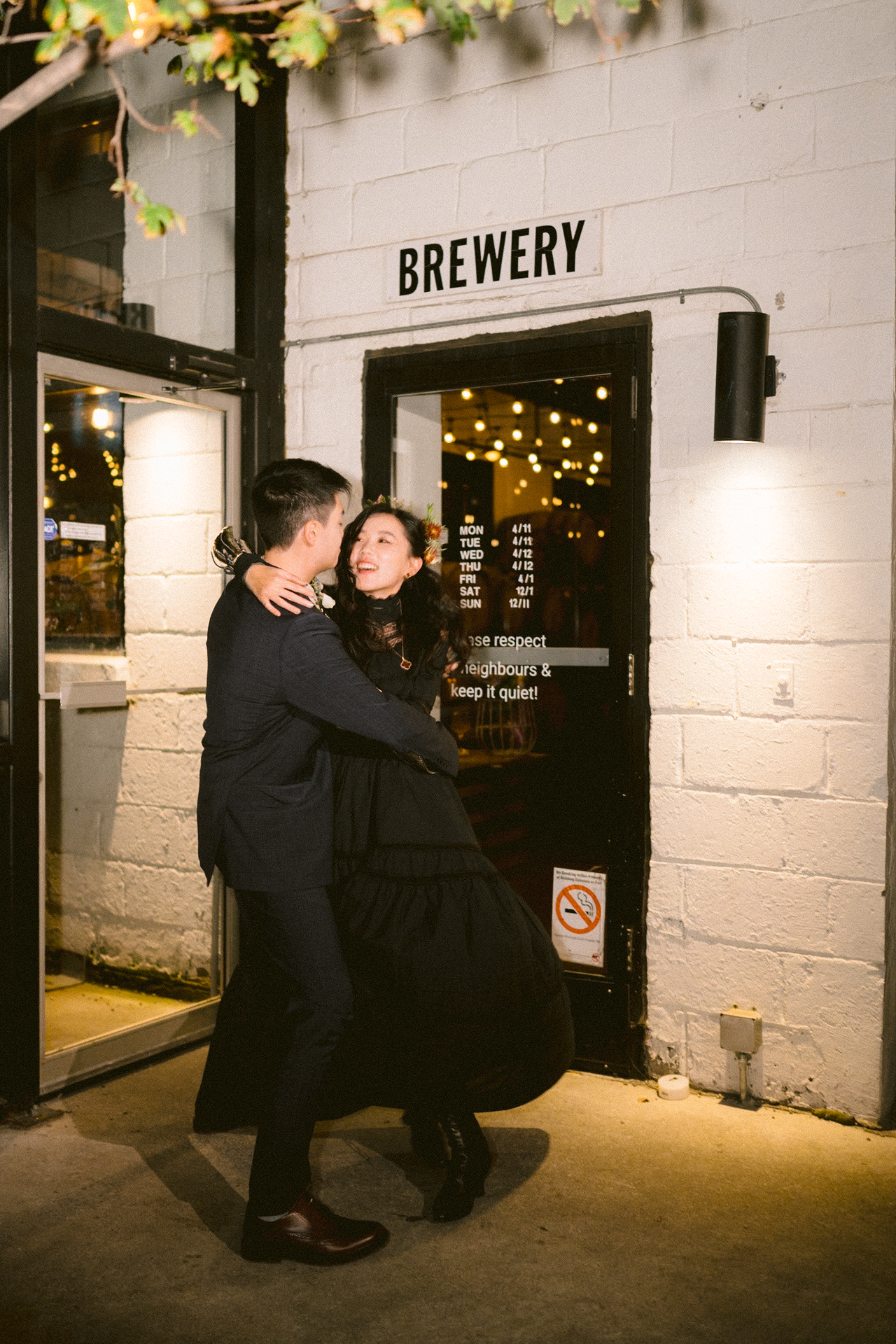 A couple sharing a romantic embrace outside a brewery at night.