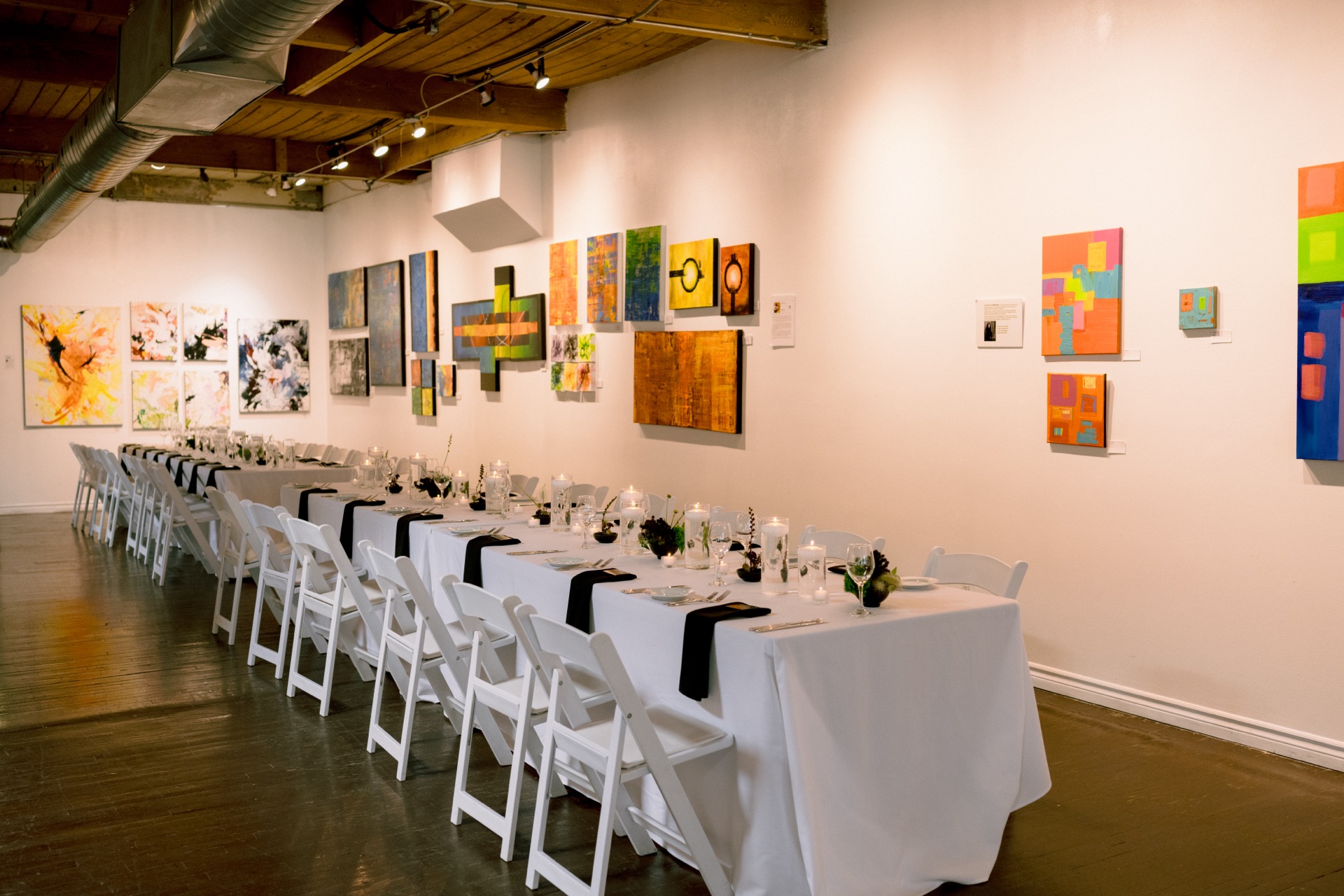 An elegantly set dinner table in an art gallery with paintings displayed on the wall.