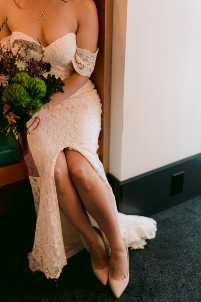 Bride in an elegant white dress holding a bouquet, seated and showing off her shoes.