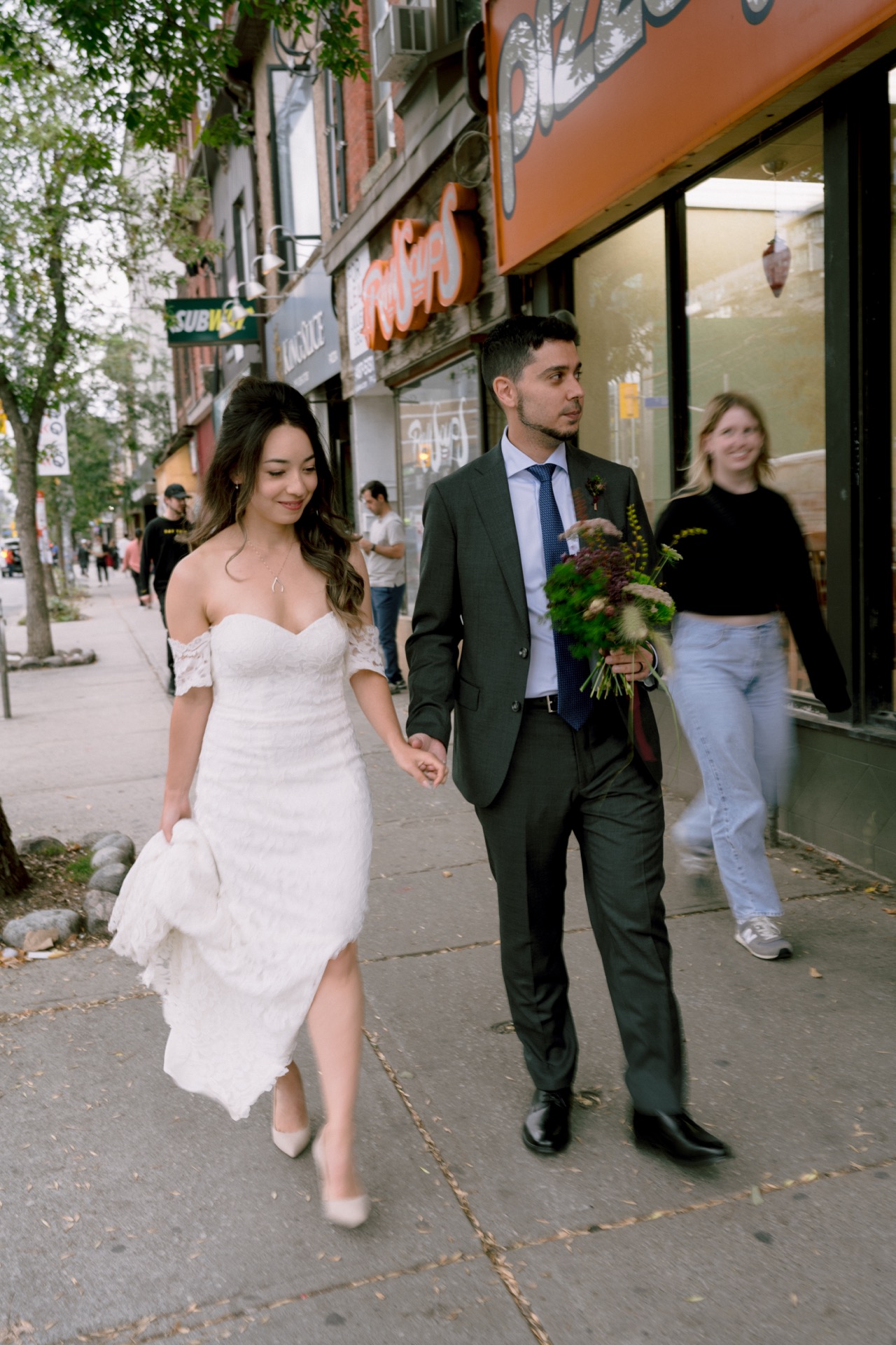 Couple in wedding attire holding hands while walking on a city sidewalk