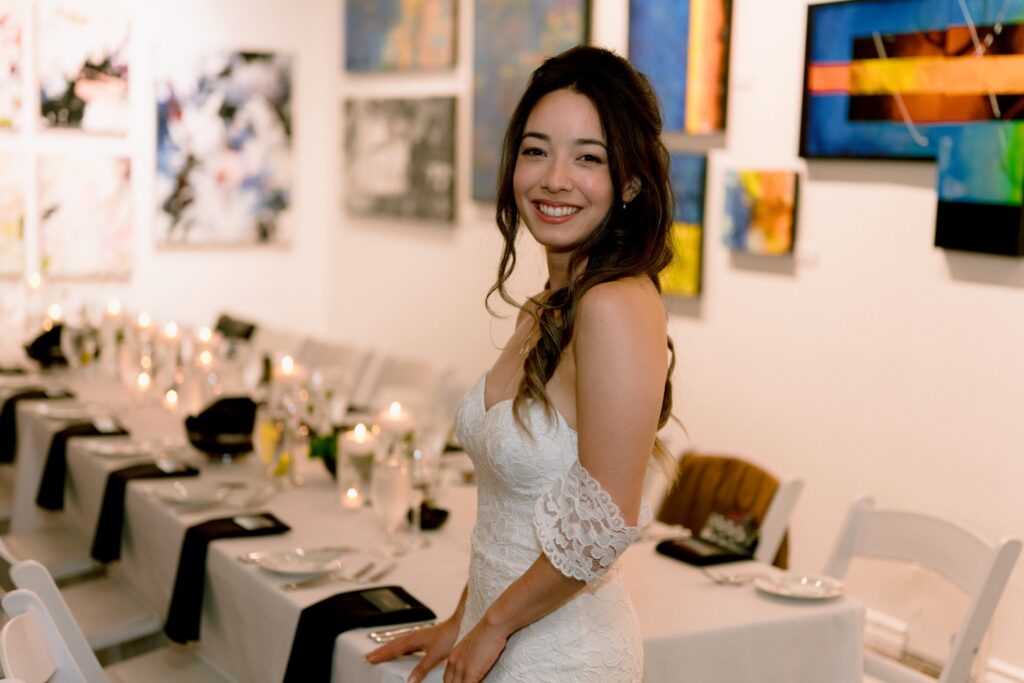 A bride in a white dress standing beside a table set for a formal event.